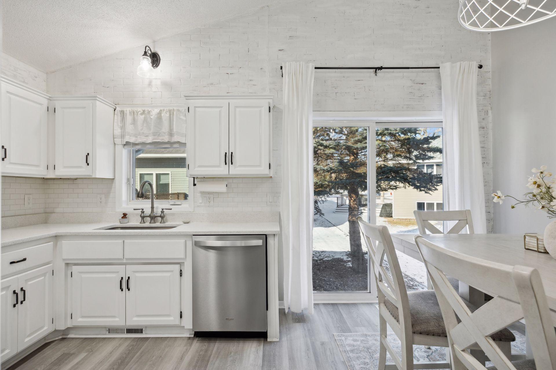 16x12 Main Level Kitchen updated with refaced white cabinetry in 2020, New dishwasher in 2024, new quartz countertops and backsplash, Fresh paint, new flooring, and white trim. North-facing windows and a sliding glass door to the side yard.