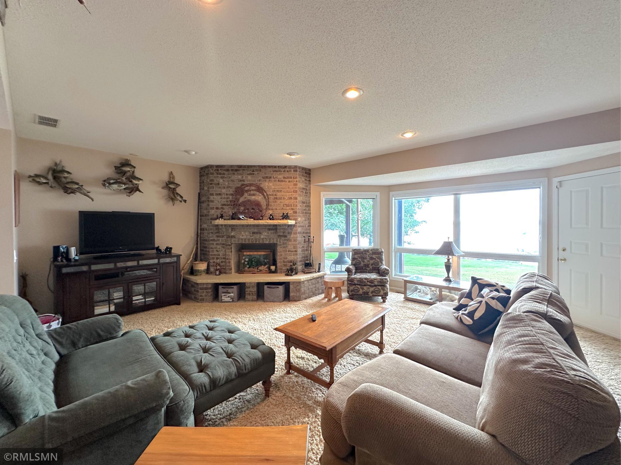 A brick fireplace anchors the space, creating a warm and inviting focal point for gatherings with lakeside views.