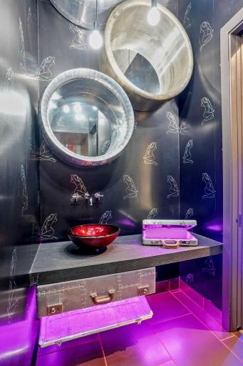 This sultry black-walled retreat channels the golden age of aviation with vintage aviator suitcases and gleaming metallic mirrors, reflecting like airplane windows into another dimension.