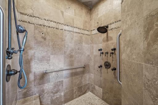walk into the custom travertine shower with dark fixtures, body jets and rain shower options.