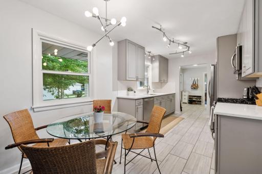 Luxurious kitchen with painted cabinetry, stainless appliances, tiled floor and quartz countertops, with views of backyard and mudroom visible in background.