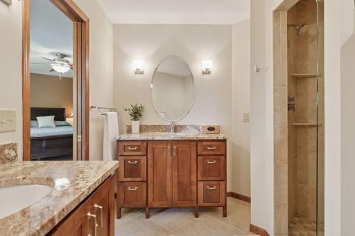 The spa-like primary bathroom offers a luxurious retreat with dual custom vanities complete with built-in shelving for ample storage, radiant heated tile floors for added comfort, and a spacious walk-in tiled shower designed for relaxation and style.