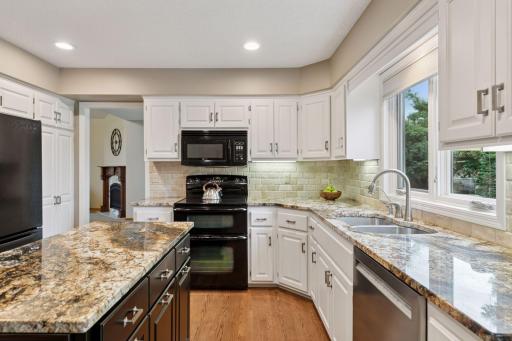 Beautifully designed kitchen featuring granite countertops, crisp white cabinetry, a central island, and rich hardwood flooring that flows seamlessly through the kitchen and dining area.