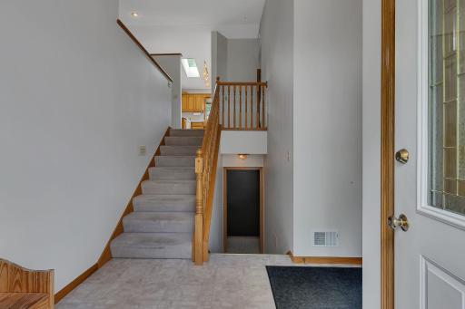 Classic split-level entry with natural wood accents and a decorative glass front door. The open stairway leads both upstairs and downstairs, creating a functional and inviting transition space.