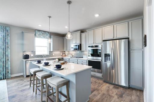 The kitchen is home to a large center island complete with quartz countertops, stainless appliances, including double ovens and a luxurious gas cooktop. *Pictures are of model, actual colors in home may vary.