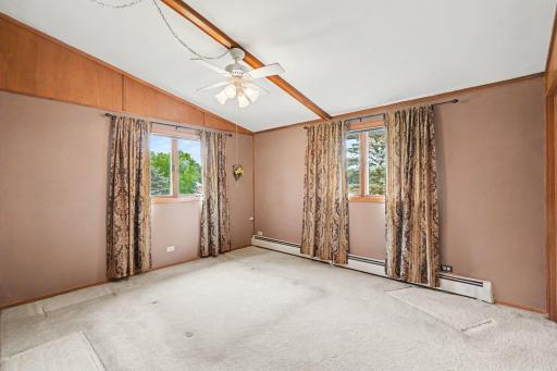 Spacious primary bedroom filled with natural light from two large windows overlooking the backyard. Features a charming wood ceiling beam, ceiling fan, and dual closets to handle all your storage needs with ease.