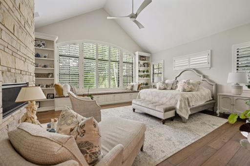 Primary bedroom with vaulted ceiling, a large arch window with custom shutters, and a stone gas fireplace