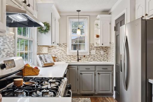 Stunning Quartz countertops with a custom tile backsplash, white enamel upper cabinets with crown molding contrasting with grey enamel lower cabinetry.