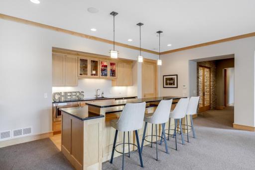 Lower level bar with sink, wine cooler beverage fridge, storage under island with matte granite countertops