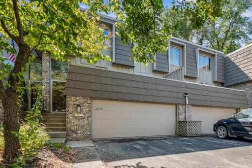 Attractive multi-level townhome featuring a brick façade, updated siding, and a two-car garage. Mature trees provide shade and curb appeal.