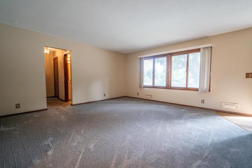 Spacious living room with new carpet fresh paint and beautiful hardwood floors underneath. There is a hall closet next to the front door to the right of this photo