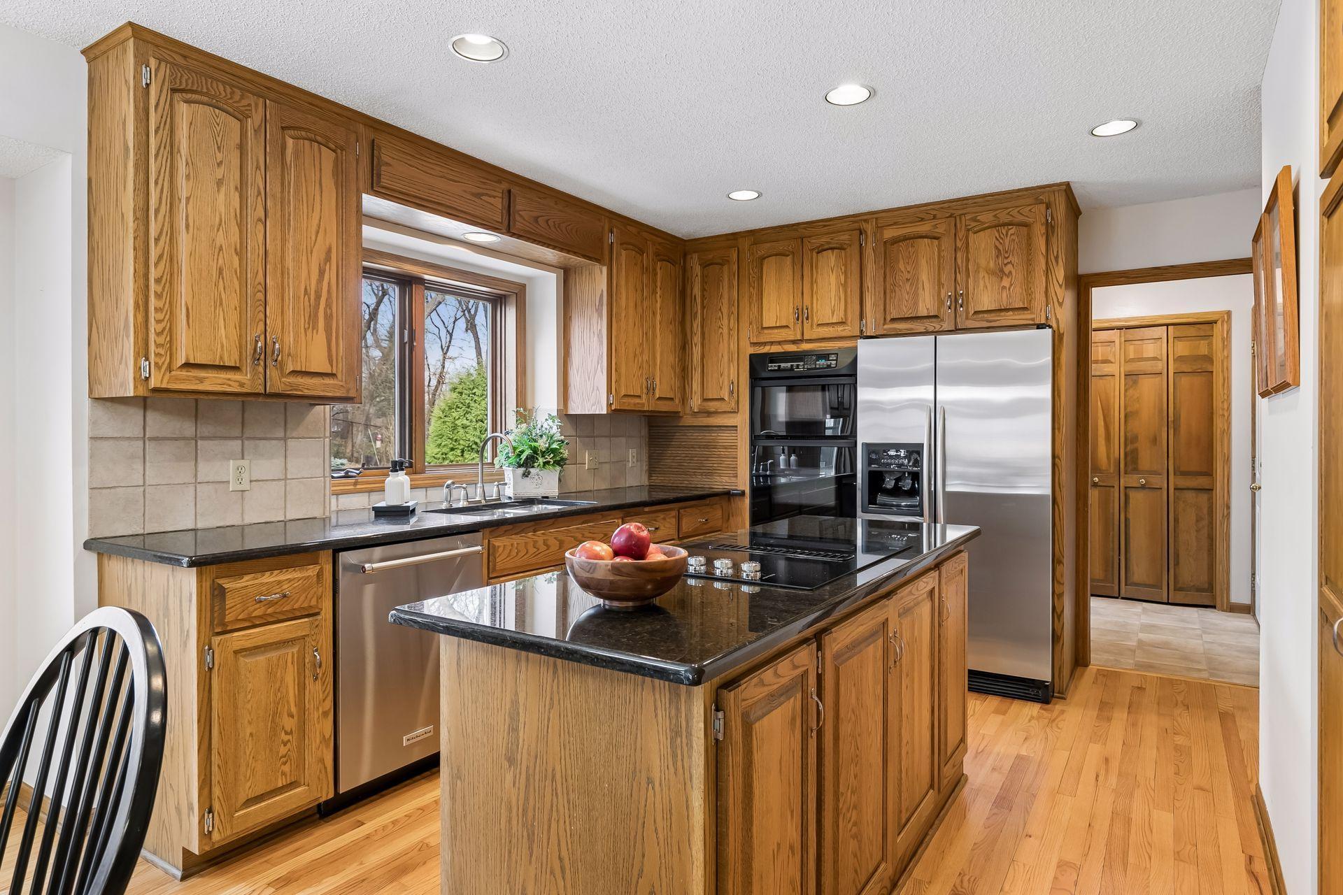 Kitchen with granite countertops, wall oven and microwave, center island cooktop, tiled backsplash & abundant cabinetry