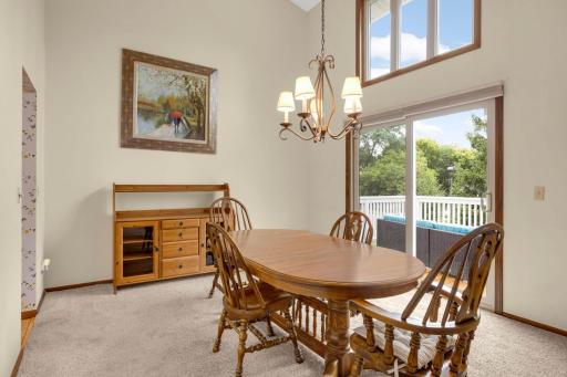 Dining area with high vaulted ceilings and direct access to a private deck overlooking green space.