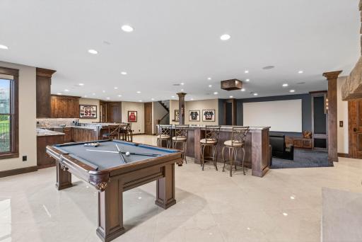 The adjoining recreation room adds more bar seating and a fireplace set against a striking stone accent wall, creating a warm and welcoming space to gather.