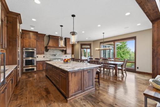 The ten-foot center island with breakfast bar seating stands as the centerpiece of the kitchen. The dining area, framed by windows and statement lighting, creates an inviting setting that moves with ease from everyday meals to entertaining.