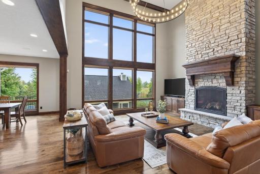 The entry sets the stage with impressive custom double doors opening into a soaring two-story great room. Floor-to-ceiling windows frame tranquil views, while a dramatic stone fireplace anchors the space.