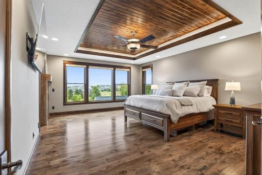 Upstairs in the main home, the primary suite is a true sanctuary. Elegant French doors open to a bedroom crowned with an Alder wood tray ceiling and soft ambient lighting.