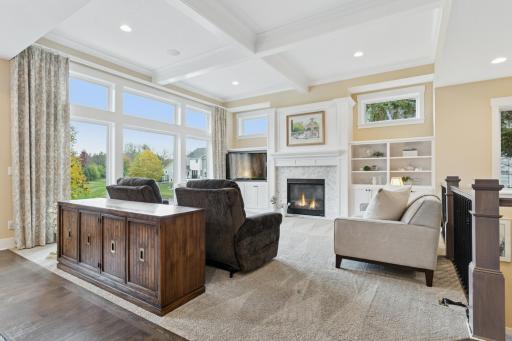 The living room showcases elegant coffered ceiling, wall of windows, and cozy gas fireplace flanked by built-ins
