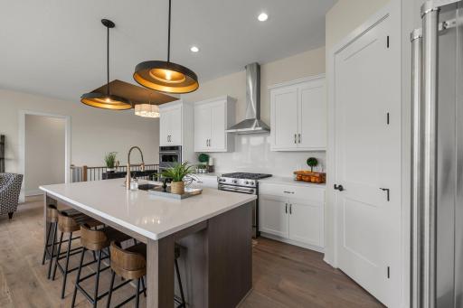 It features a large center island with quartz countertops, soft-close cabinetry, a gas range with hood vent, and a built-in wall oven.