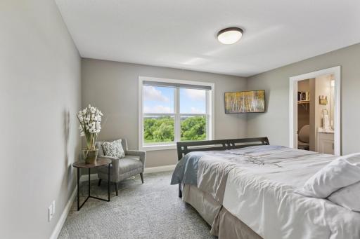 The first upper level bedroom features plush carpeting, a neutral palette, and abundant natural light streaming through the large window.