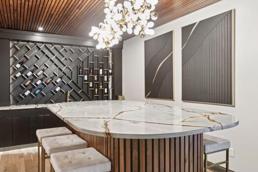 Stunning custom bar table and wet bar with abundant wine storage, quartzite countertops, and designer lighting.