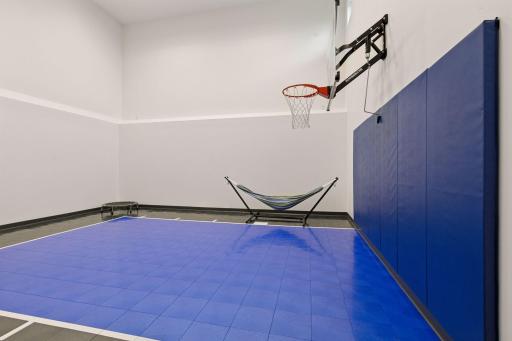 Private indoor sports court with basketball hoop and protective wall padding for year-round active entertainment.