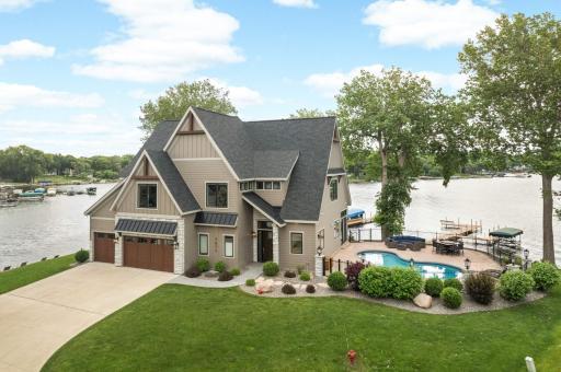 Custom home featuring a wide concrete driveway with ample parking, a spacious 3-car garage with upgraded wooden garage doors, and a beautifully maintained yard that enhances its striking exterior design.