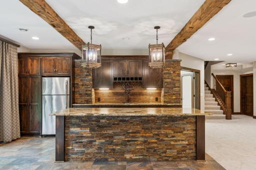 The walk-behind bar features rich wood cabinets, striking stack stone detail, and a copper sinkâan artful blend of style and function that sets the stage for effortless entertaining.