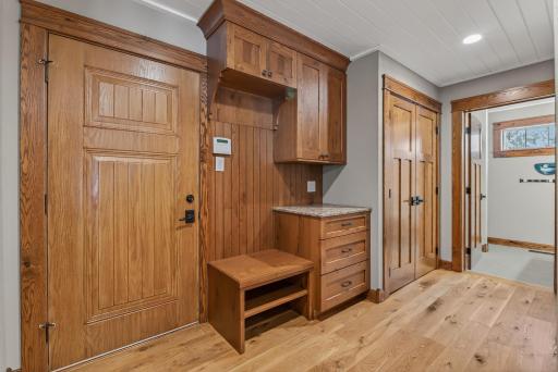 The space flows into a functional mudroom with durable wood flooring, bench seating, cabinetry, counters, multiple closets, and access to the attached 3-car garage.