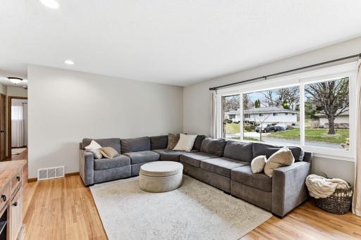 Bright and inviting living room featuring hardwood floors, recessed lighting, and a large front window that fills the space with natural light. The layout flows seamlessly toward the dining area and kitchen.