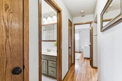 Hallway connecting bedrooms and bathroom, featuring hardwood floors and a simple, functional layout.