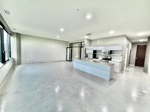 This elegant open-concept space seamlessly blends the living area with a modern, sleek kitchen, offering a sophisticated and airy ambiance perfect for both entertaining and everyday living.