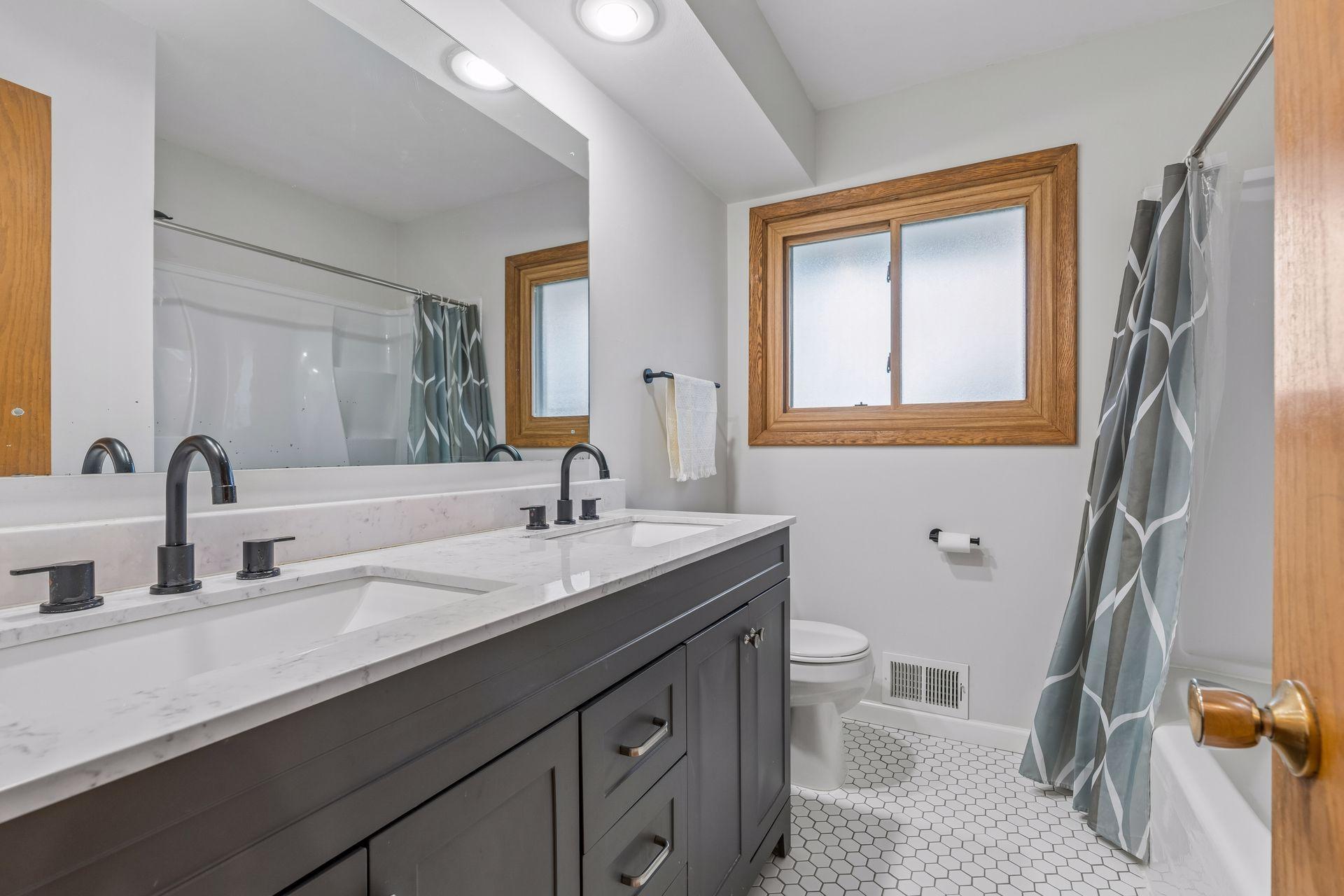 Modern and sleek renovated in main floor full bath in 2022 - dual vanity, hexagon tile flooring, and fixtures.