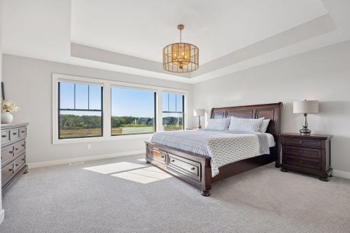 The upper-level primary suite boasts sweeping wetland views and a partially recessed ceiling adorned with a striking pendant light