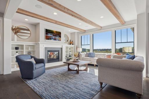 The living room blends warmth and elegance with wood ceiling beams, a gas fireplace, custom built-ins, and serene views of the wetlands