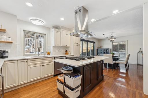 Beautifully updated kitchen featuring custom cabinetry, a center island with cooktop and hood, quartz countertops, and an open flow into the dining area with abundant natural light.