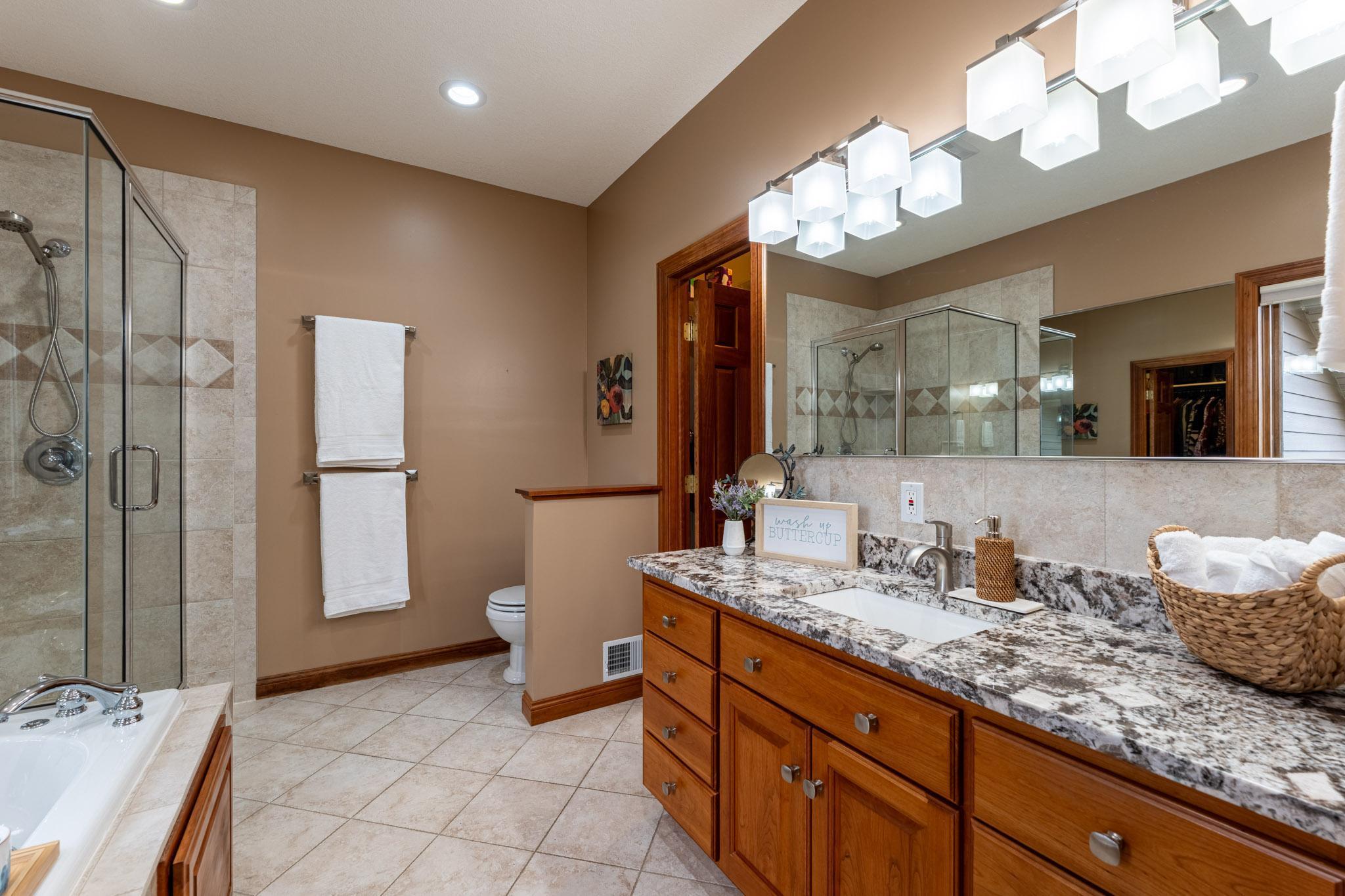 The en-suite bath with granite counters, tiled shower & flooring, soaking tub, and spacious walk-in closet.