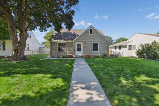 Charming curb appeal with fresh landscaping, mature shade tree, and a welcoming concrete walkway leading to the front entry.