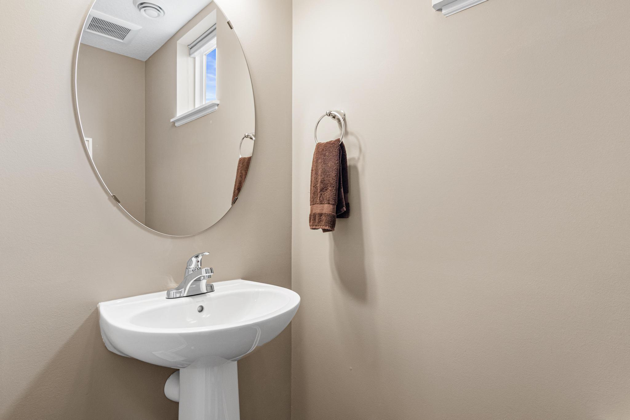 Convenient main-floor powder room featuring a classic pedestal sink and an elegant oval mirror. This bright and clean space is perfectly situated for guests, showcasing neutral tones and a well-placed window for natural light.