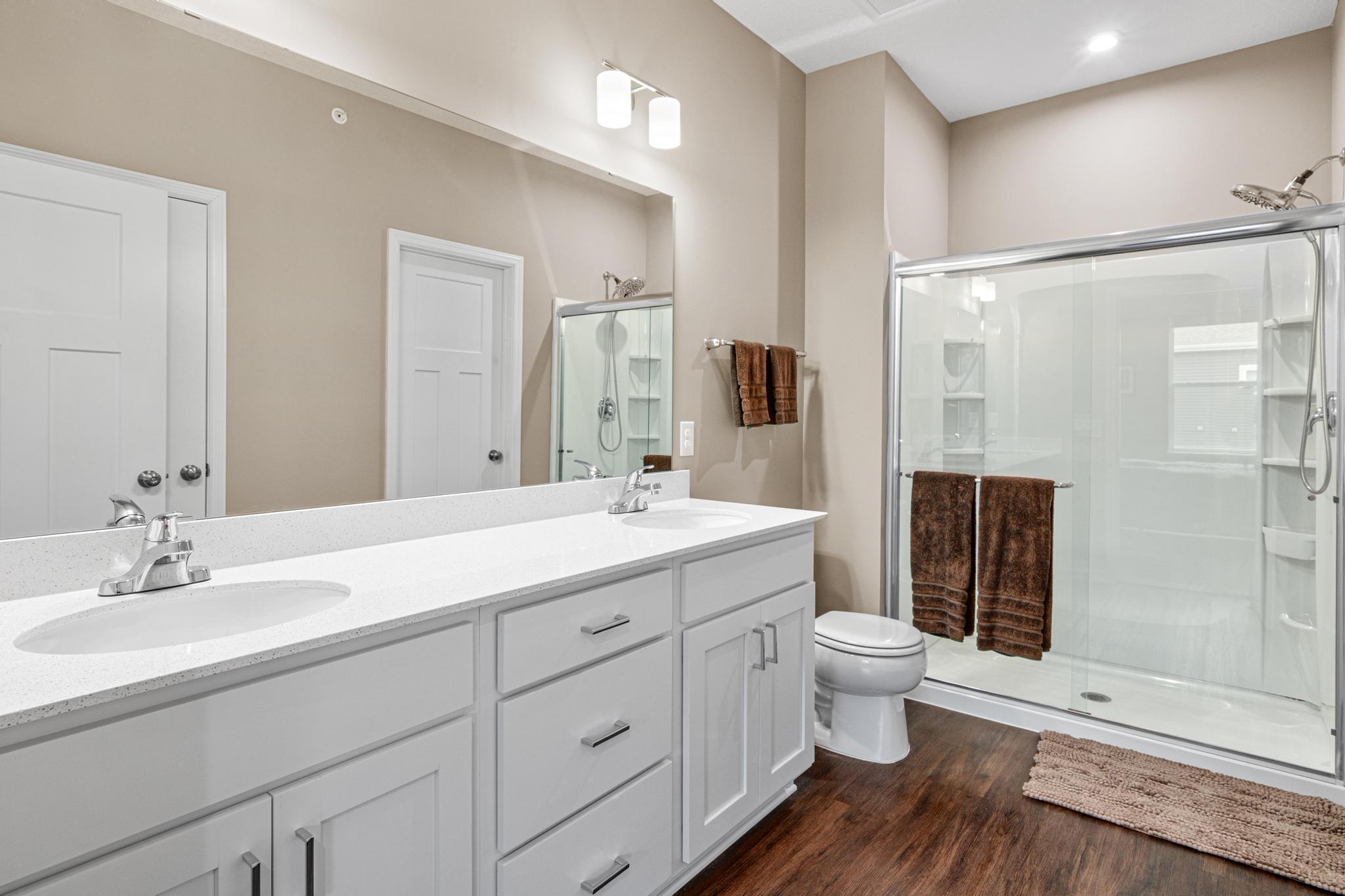 Luxurious primary ensuite featuring a long double vanity with quartz countertops, ample cabinet storage, and a large mirror. This bright space includes a spacious walk-in shower and beautiful flooring, offering a private, spa-like experience.