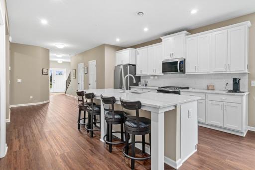 Gourmet kitchen showcasing stunning white cabinetry and a large center island. The expansive quartz countertop comfortably accommodates seating for four stools, creating a perfect hub for casual dining and entertaining.