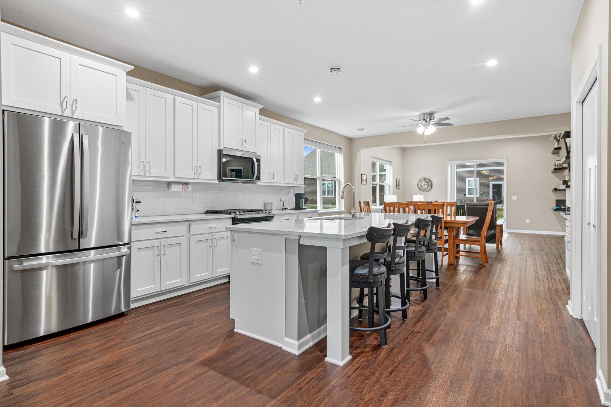 Gourmet kitchen featuring quartz countertops and a large center island, offering a seamless flow into the dining and living areas. Highlights include premium flooring throughout the open-concept main level and abundant natural light from the patio do