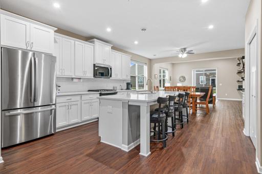Gourmet kitchen featuring quartz countertops and a large center island, offering a seamless flow into the dining and living areas. Highlights include premium flooring throughout the open-concept main level and abundant natural light from the patio do