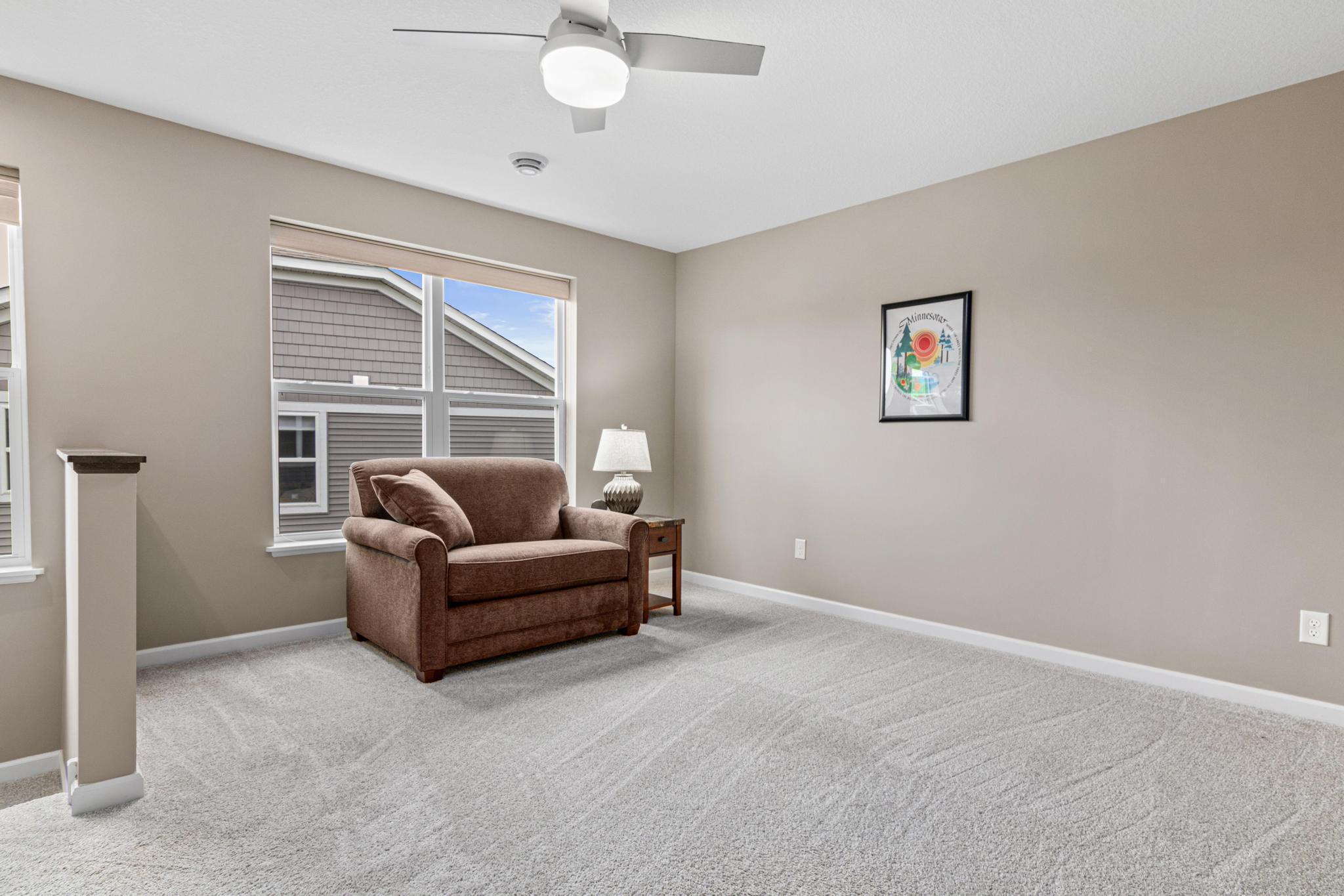 Spacious upper-level loft featuring plush carpeting, a ceiling fan, and two large windows that flood the area with natural light. This versatile space offers a perfect secondary living zone, hobby area, or quiet retreat for guests.