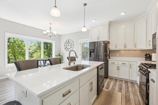 Bright and functional kitchen designed for everyday living—featuring crisp white cabinetry, sleek quartz counters, soft-close drawers, and a center island ideal for cooking or gathering. Large windows frame views of lush greenery