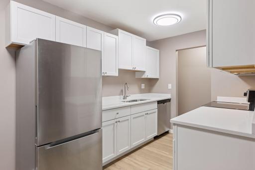 Professionally remodeled kitchen with stainless-steel appliances, quartz countertops, white cabinetry and new flooring.