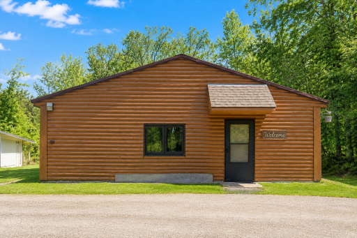 Welcoming front exterior of the log home with sunny curb appeal, mature trees, and peaceful Aitkin acreage surrounding the property.