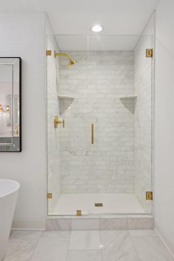 Beautifully appointed shower tile with shelves, gold accent hardware and plumbing fixtures.