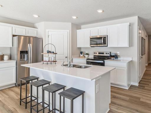 Modern white kitchen with quartz countertops and island. Picture of previously built model home; finishes, selections, and colors to vary.