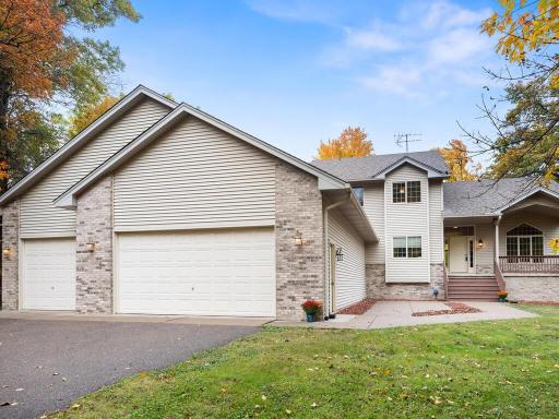 Stunning two-story home with a welcoming front porch, brick accents, and a spacious three-car garage set on a peaceful wooded lot.